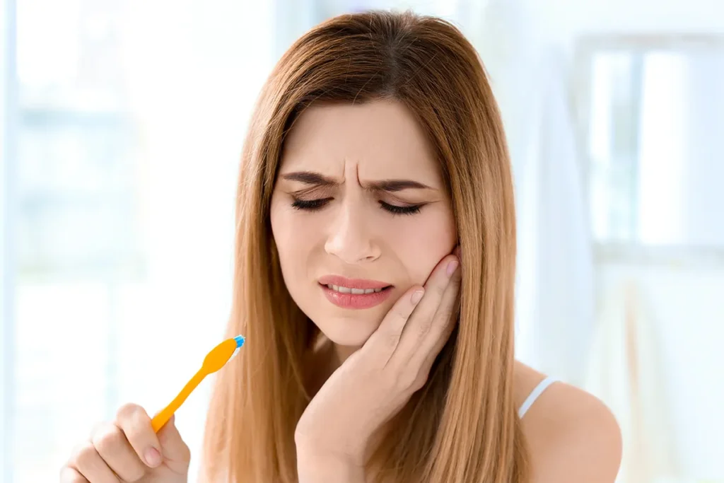 woman-with-toothache-holding-toothbrush-in-bathrooM